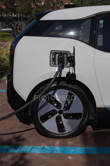 Электрический автомобиль заряжается на зарядной станции в солнечный день — стоковое фото