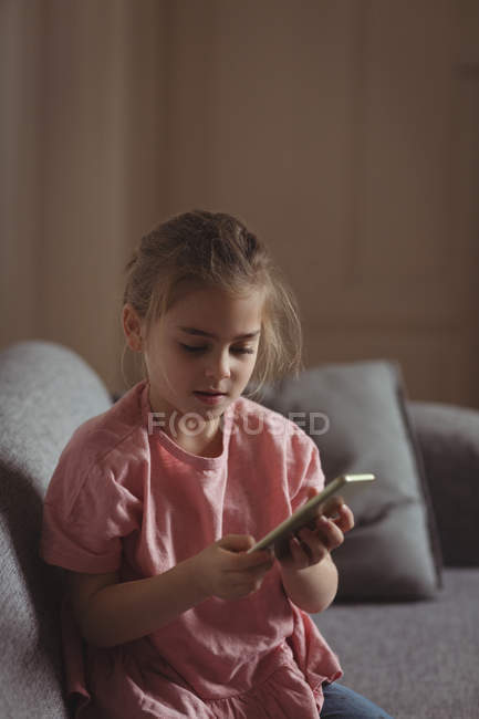 Маленькая девочка с помощью мобильного телефона в гостиной на дому — стоковое фото