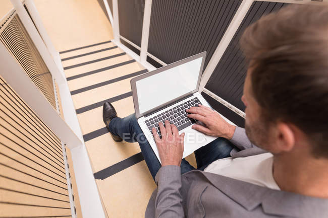 Empresário usando laptop na escada no escritório — Fotografia de Stock