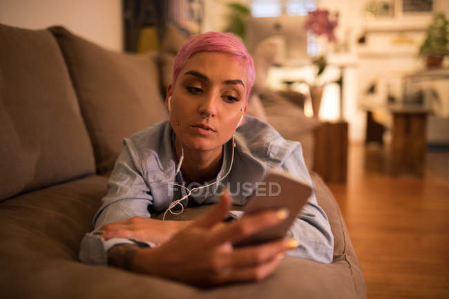 Stylish woman listening music on mobile phone in living room at home — Stock Photo