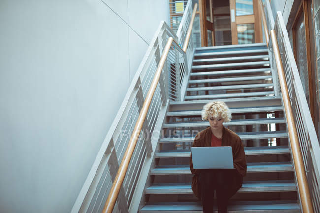 Jovem mulher usando laptop na escada na biblioteca — Fotografia de Stock