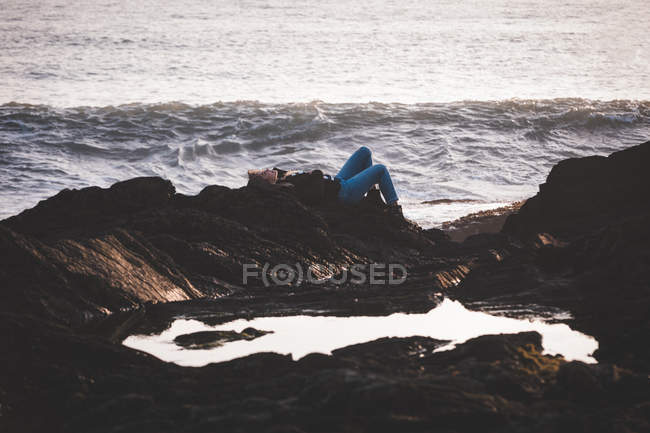 Frau liegt in der Abenddämmerung auf einem Felsen am Strand — Stockfoto