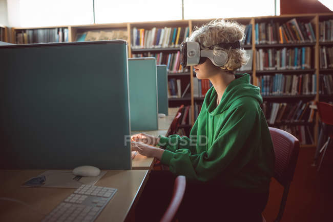 Jovem mulher usando fone de ouvido realidade virtual com computador na biblioteca — Fotografia de Stock