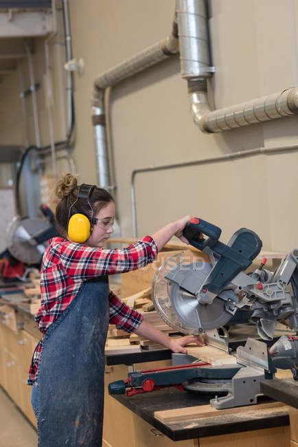 Female carpenter using grinder cutting machine at workshop — Stock Photo