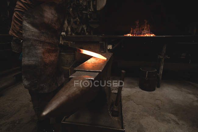 Blacksmith examining a hot metal rod in workshop — Stock Photo