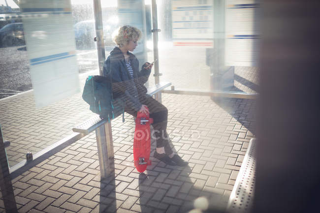 Junge Frau benutzt Handy an Bushaltestelle — Stockfoto