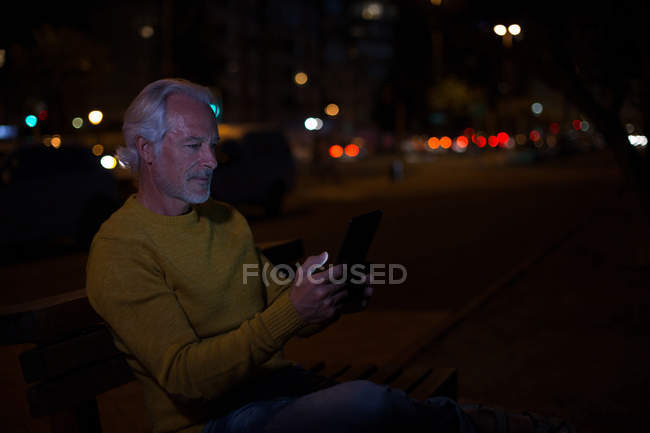Hombre mayor usando tableta digital en la ciudad por la noche - foto de stock