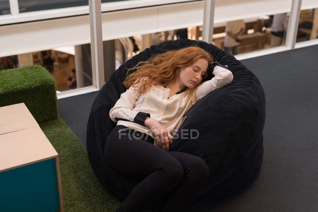 Женщина исполнительный расслабляющий на бобовый мешок в офисе — стоковое фото