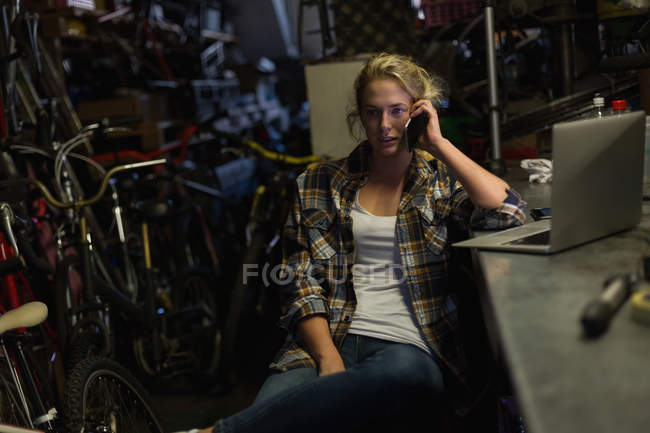Mecânico feminino falando no celular na oficina — Fotografia de Stock