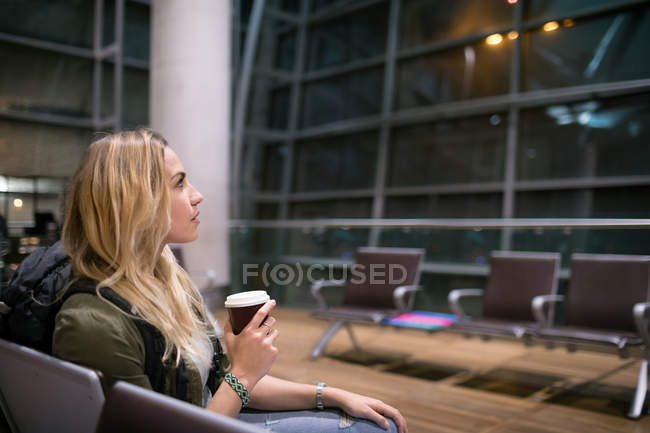 Mujer tomando café mientras espera en la sala de espera en la terminal del aeropuerto - foto de stock
