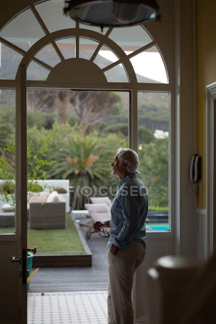 Задумчивый пожилой человек, стоящий у двери дома — стоковое фото