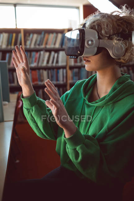 Jeune femme utilisant casque de réalité virtuelle dans la bibliothèque — Photo de stock