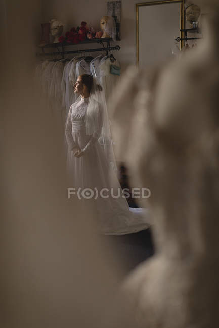 Jeune mariée en robe de mariée debout près de la fenêtre à la boutique — Photo de stock