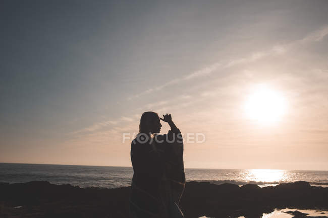 Silhouette of woman standing on a beach at dusk — Stock Photo