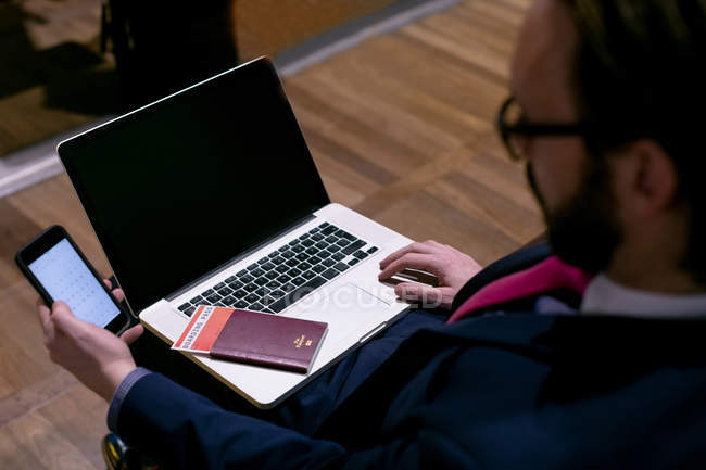 Бізнесмен використовує мобільний телефон під час роботи на ноутбуці в зоні очікування вдома — стокове фото