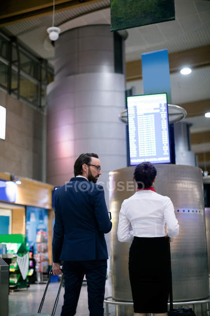 Geschäftsmann und Frau blicken auf Abflugtafel am Flughafen — Stockfoto