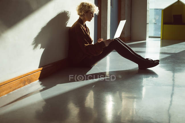 Молода жінка, використовуючи ноутбук у бібліотеці, сидить на підлозі — стокове фото