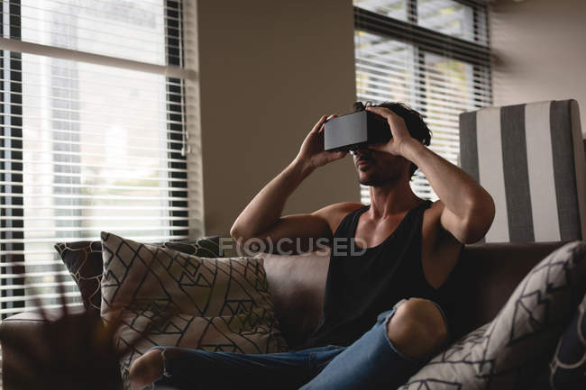 Человек, использующий гарнитуру виртуальной реальности в гостиной дома — стоковое фото