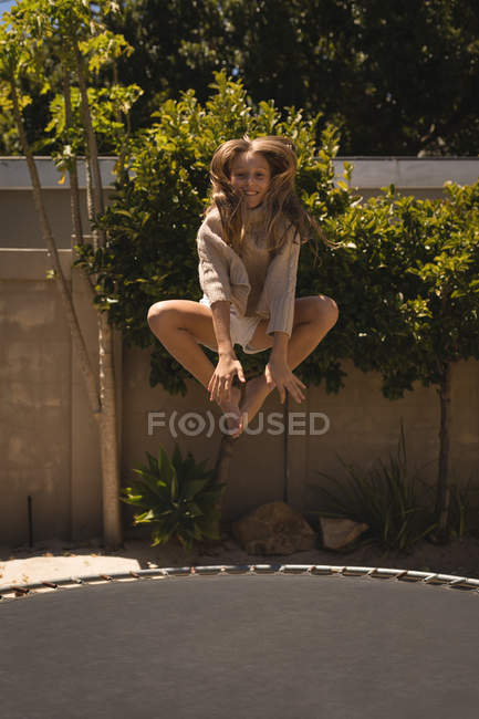 Girl jumping on a trampoline in the garden on a sunny day — Stock Photo
