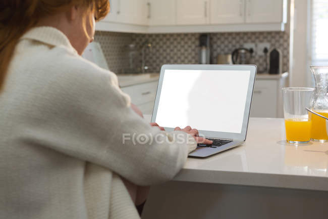 Вид сзади женщины, использующей ноутбук на кухне дома — стоковое фото