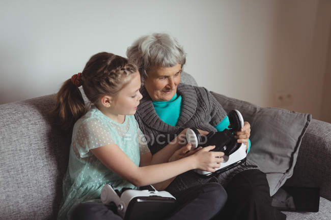 Бабушка и внучка держат гарнитуру виртуальной реальности в гостиной дома — стоковое фото