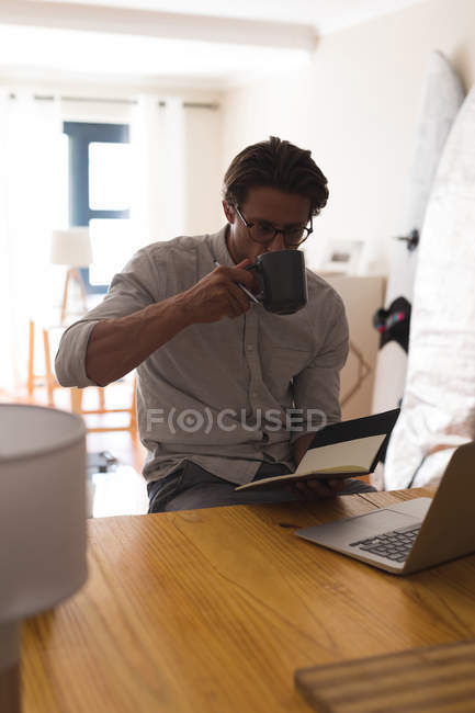 Mann trinkt Kaffee, während er zu Hause Tagebuch führt — Stockfoto