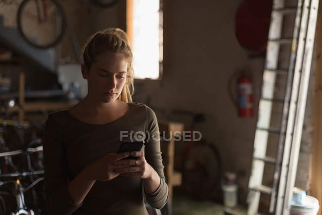 Junge Mechanikerin benutzt Handy in Werkstatt — Stockfoto