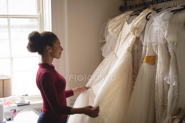 Mulher selecionando vestido de noiva de cabides de roupas na boutique — Fotografia de Stock