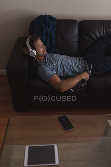 Homme écoutant de la musique sur écouteurs dans le salon à la maison — Photo de stock