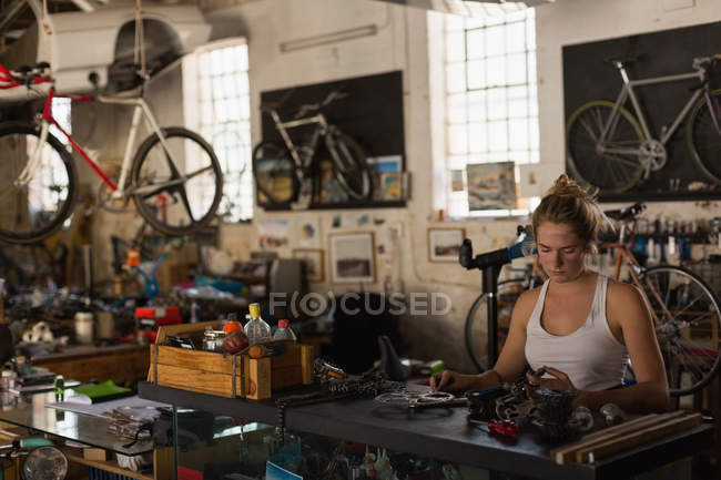 Mecânico feminino examinando peças de bicicleta na oficina — Fotografia de Stock