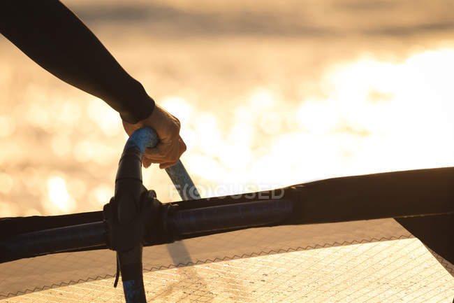 Imagem cortada de surfista segurando um papagaio na praia ao entardecer — Fotografia de Stock