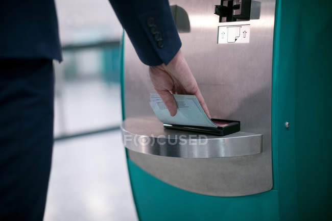 Sección media del hombre de negocios utilizando la máquina de billetes de avión en el aeropuerto - foto de stock
