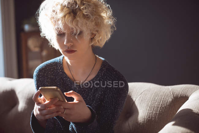 Mujer usando teléfono móvil en la sala de estar en casa - foto de stock