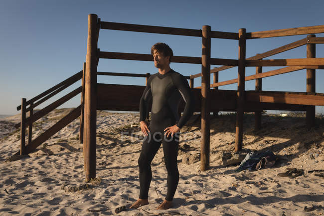 Удумливий чоловічий серфер, що стоїть у купальнику на пляжі — стокове фото