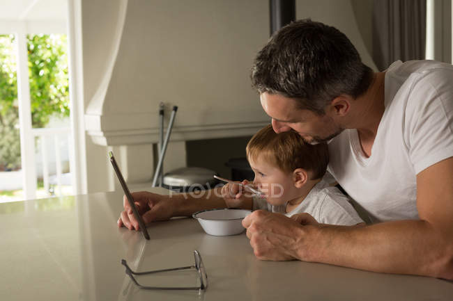 Отец и сын завтракают, используя цифровой планшет дома — стоковое фото