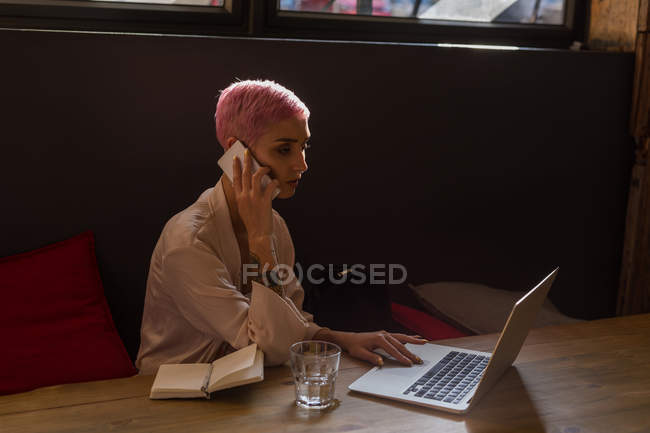 Стильна жінка використовує ноутбук, коли чоловік розмовляє на мобільному телефоні в ресторані — стокове фото