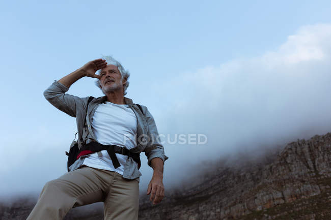 Senior hiker shielding eyes on a mountain — Stock Photo