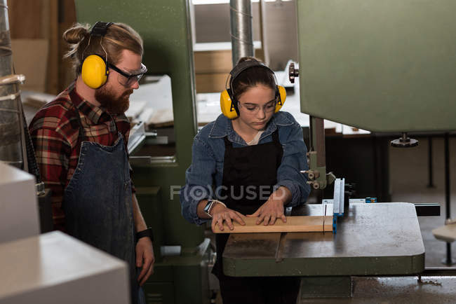 Carpinteiros masculinos e femininos trabalhando juntos na máquina de corte vertical na oficina — Fotografia de Stock