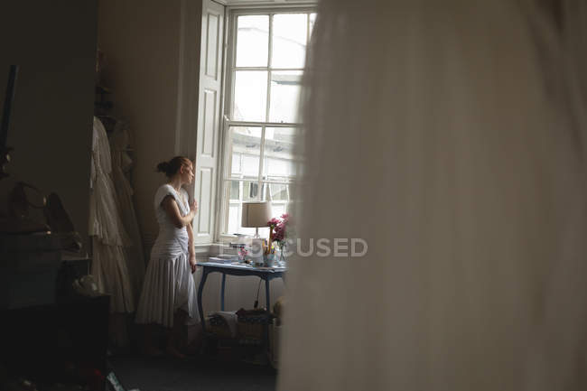 Noiva em vestido branco olhando através da janela em boutique — Fotografia de Stock