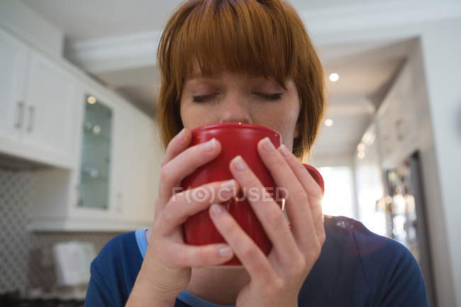 Frau trinkt Kaffee im roten Becher zu Hause — Stockfoto