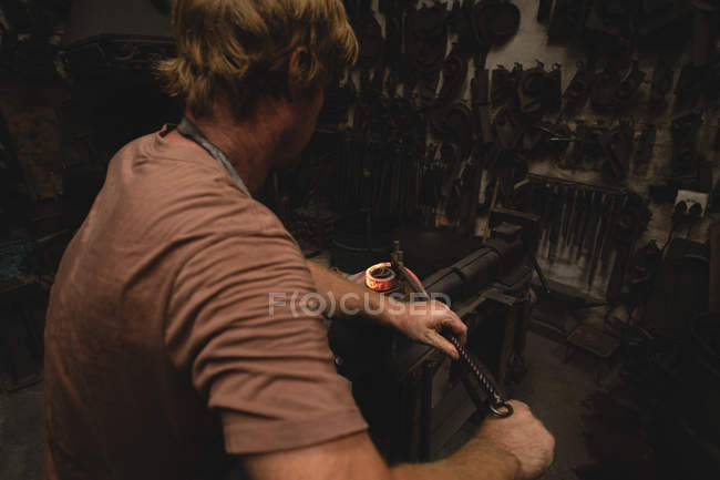 Herrero dando forma a una varilla de metal en el taller - foto de stock