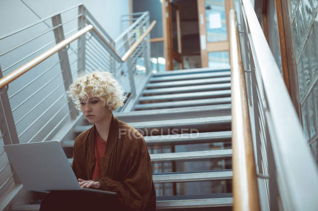 Mujer joven usando el ordenador portátil en la escalera en la biblioteca - foto de stock