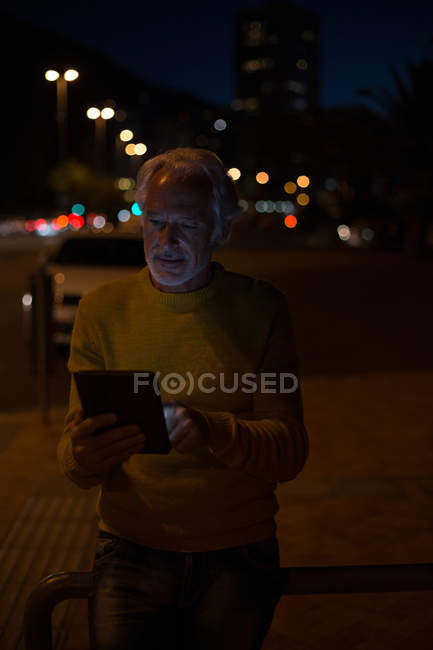 Старший чоловік використовує цифровий планшет у місті вночі — стокове фото