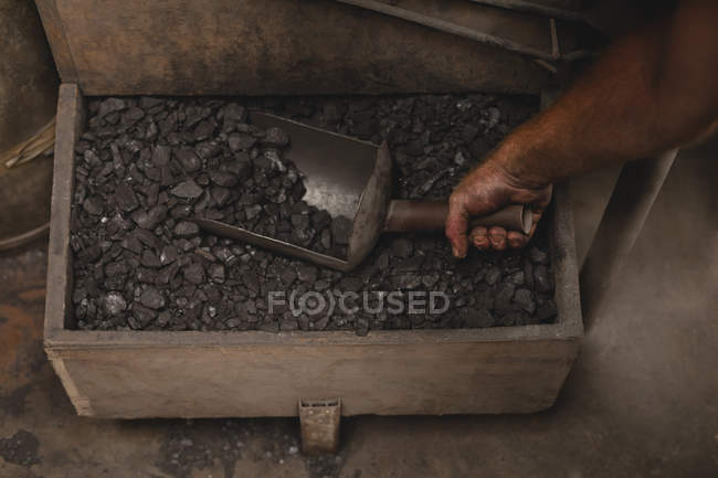 Blacksmith removing coals from box in workshop — Stock Photo