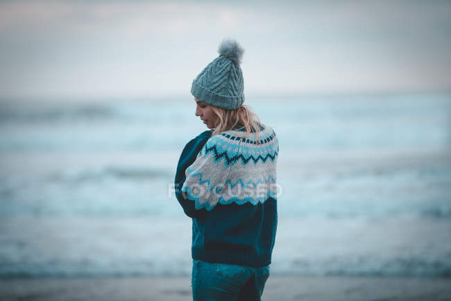 Mujer pensativa de pie en una playa al atardecer - foto de stock
