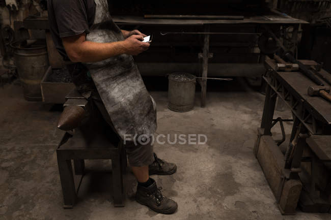 Blacksmith using mobile phone in workshop — Stock Photo