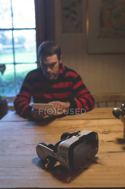 Auriculares de realidad virtual en la mesa mientras el hombre utiliza la tableta digital en casa - foto de stock