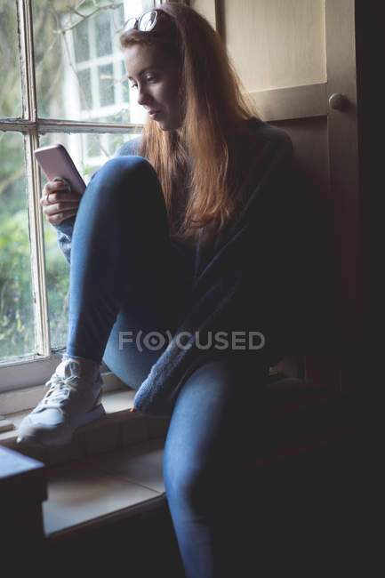 Donna che utilizza il telefono cellulare vicino alla finestra a casa — Foto stock