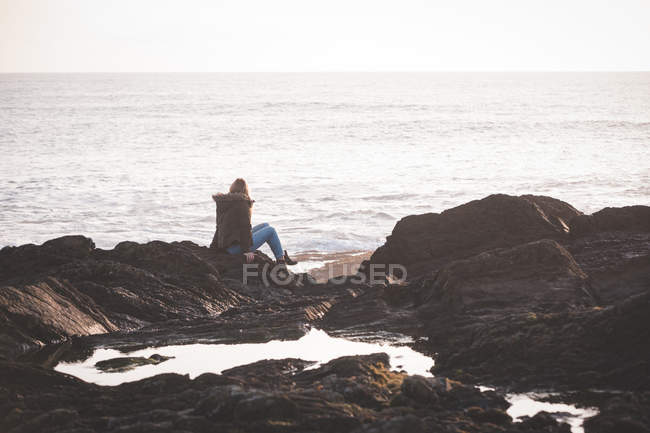 Вид ззаду жінки, що сидить на скелі на пляжі — стокове фото