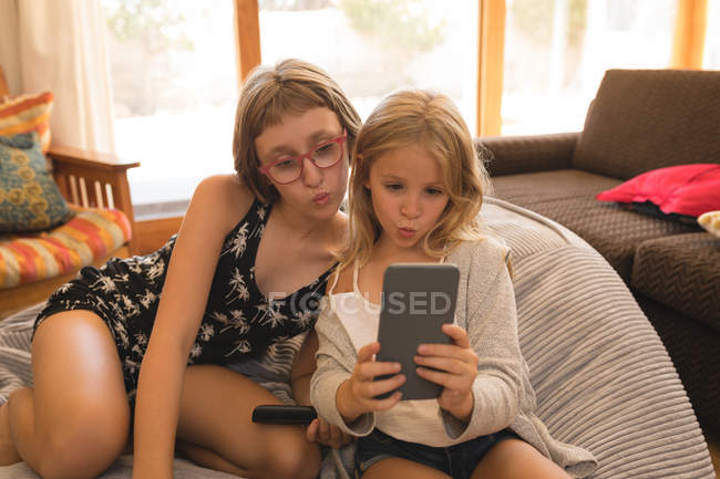 Frères et sœurs prenant selfie avec téléphone portable dans le salon à la maison — Photo de stock